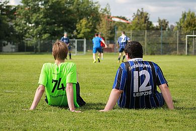 Zwei Fußballspieler sitzen auf dem Rasen und sind von hinten zu sehen
