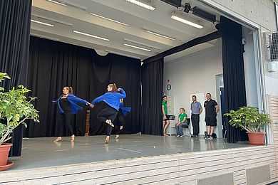 Zwei Mädchen tanzen auf einer Bühne und tragen dabei schwarze Leggins und blaue Jacken.