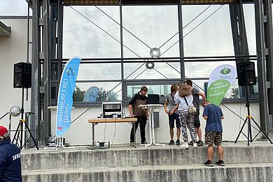 4 Jugendliche an einer Musikanlage stehend vor einer Sporthalle