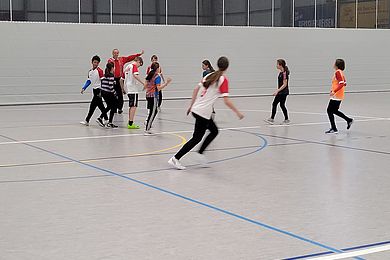 Auf dem Spielfeld in einer Halle rennen einige Spieler*innen